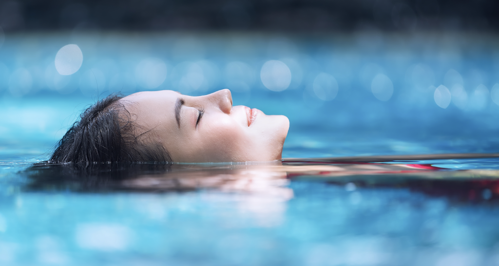Woman lying in water with eyes closed, relaxing